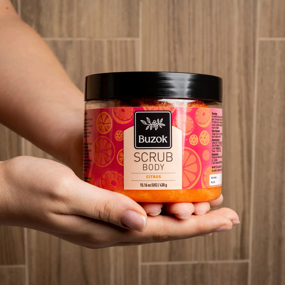 Person holding a jar of Buzok scrub body product against a tiled wall background